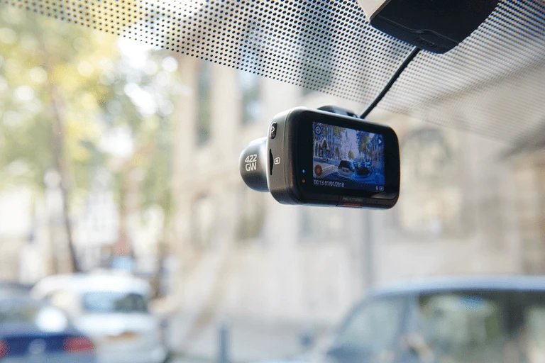 A close-up of a microSD memory card held against a blurred dash cam background.