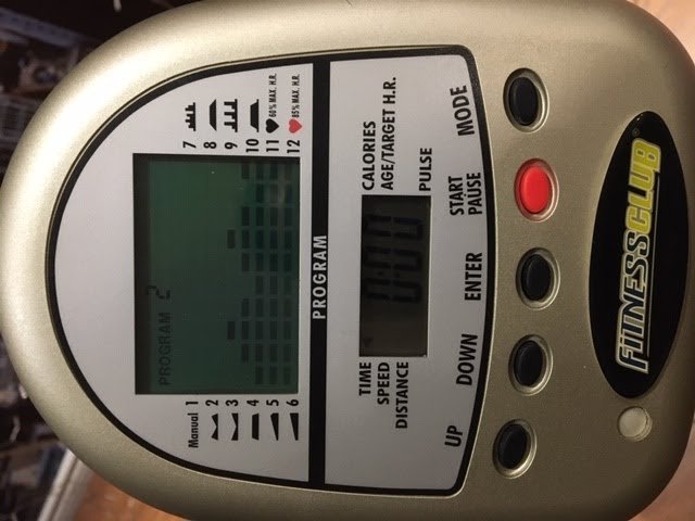 A person troubleshooting a faulty exercise bike monitor by checking the battery compartment.