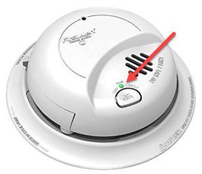 A close-up of a fire alarm blinking green to indicate active power.