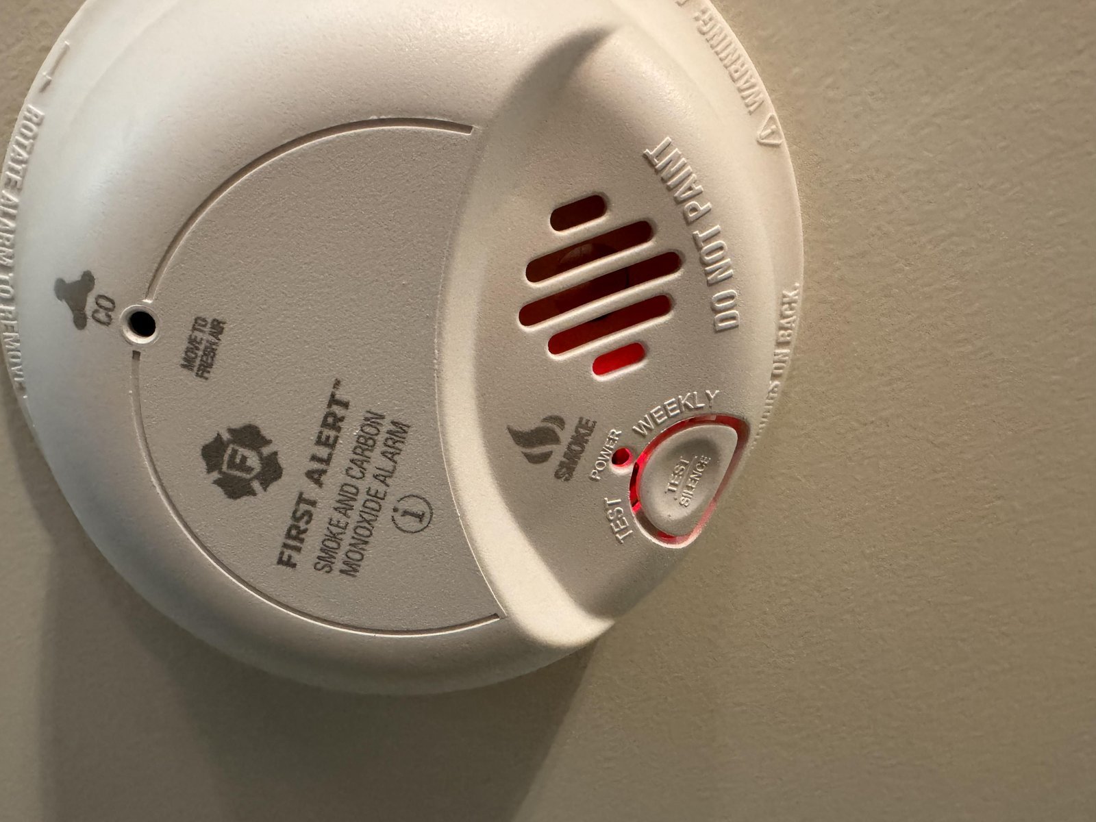 A person pressing the reset button on a smoke detector to troubleshoot the blinking light.